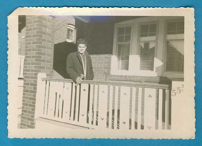 A young man stands in a porch and light shines on him.