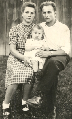 Man and woman sitting in front of a fence, a baby on their lap.