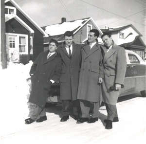 Four young men in overcoats standing on a snow-covered street.