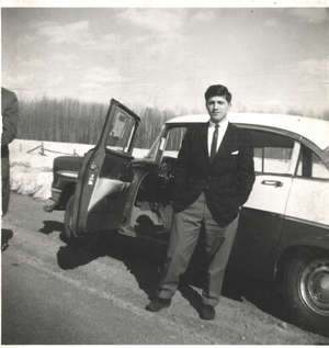 Young man standing in front of open door of car on side of the road.