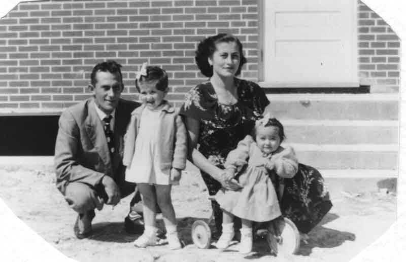 Black and white photo of young couple with two children in front of their house.