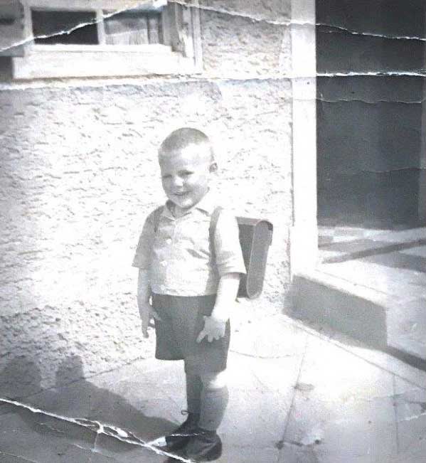Old cracked photograph of a smiling little boy with a backpack.
