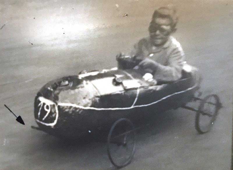 A little boy wearing goggles sits and steers his makeshift go cart.