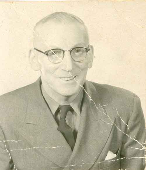 A cracked old photo of a gentleman smiling and wearing glasses.