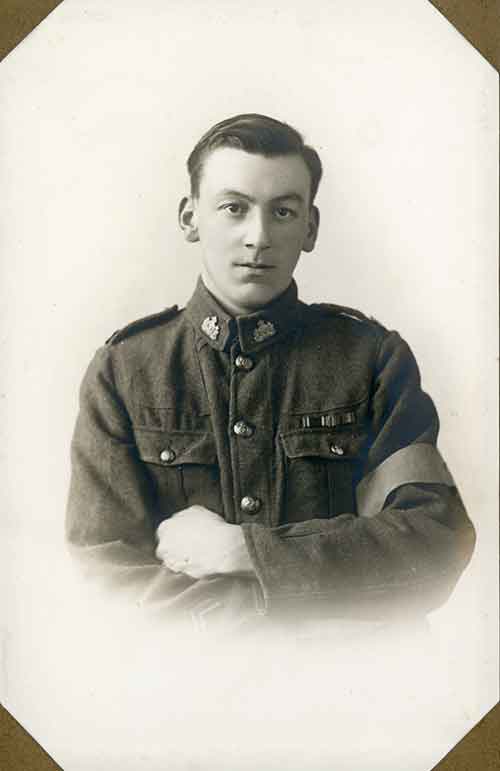 A stern looking young man in uniform stands with his arms crossed over his chest.