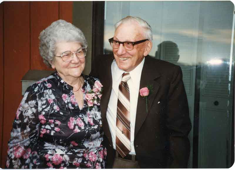 A smiling middle-aged couple stand with arms around each other.