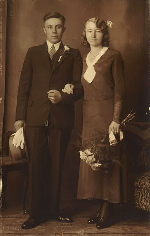 A well-dressed woman is next to a young man and holds flowers in her left hand.