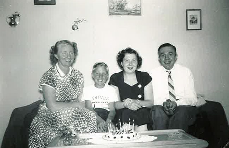 A young family is sitting on a couch with a cake on the table in front of them.