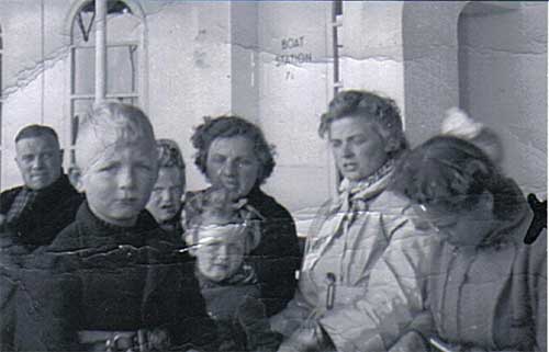 Black and white photo of three women, a man and three kids, they are sitting on a boat.