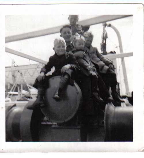 Four children with one man sitting on the deck of ship.