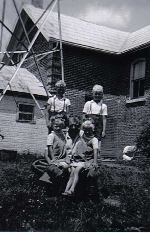 One man with four children sitting on the grass in front of a house.