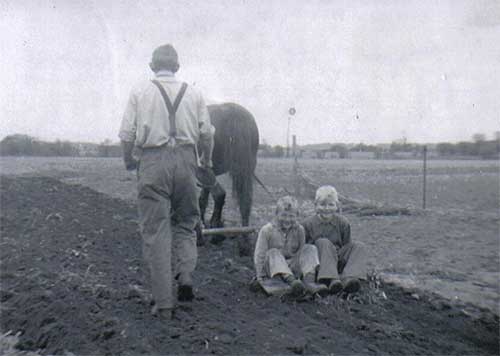 Man sows crops in a field while children watch.
