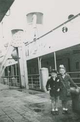 Two small children on dock with ship sitting alongside.