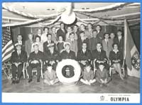 Officers of ship seated and standing for photo, behind life saver.