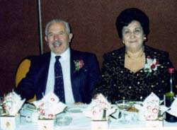 Coloured photo of older man and woman seated at a banquet table.