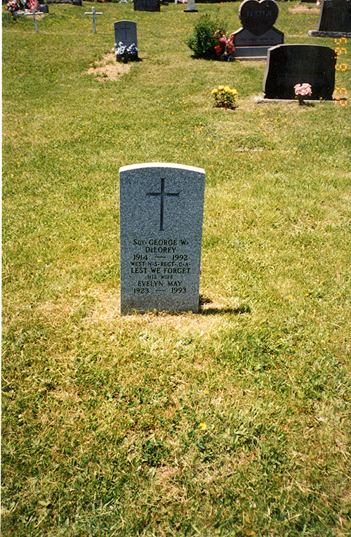 A tombstone sits in a green grass cemetery.