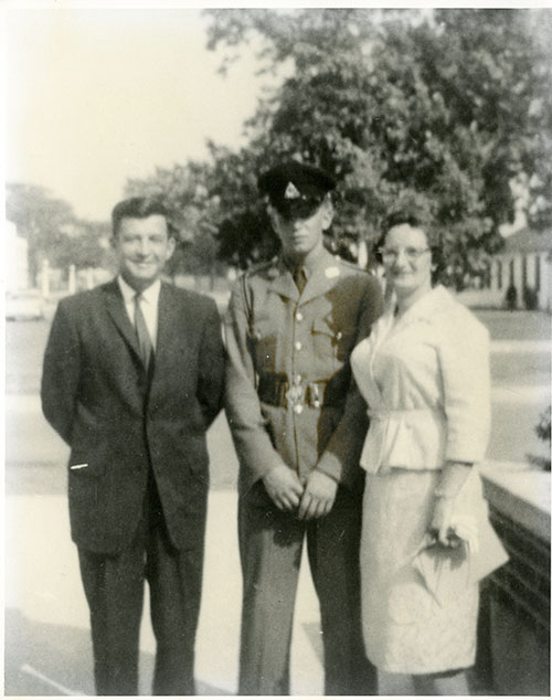 Man and woman standing with a young man in military uniform, a tree can be seen in the background.