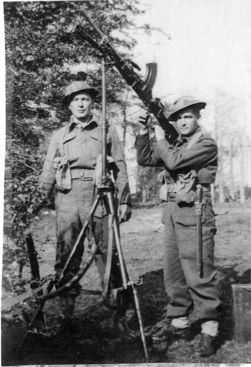 Two young men in military uniform hold guns and pose for the camera.