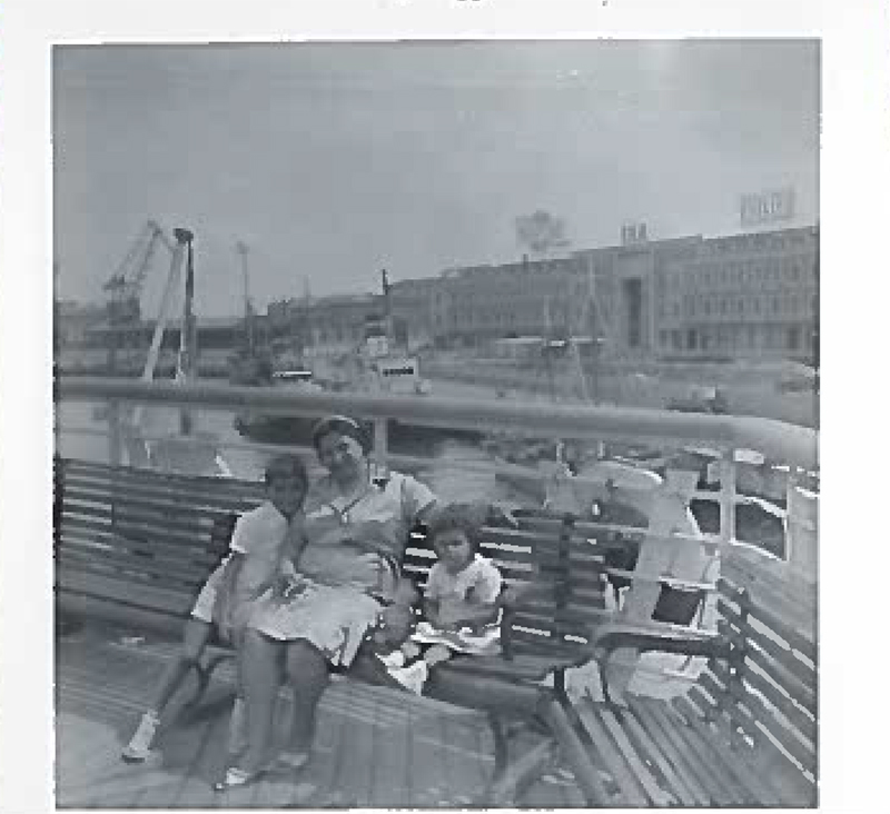 A woman is sitting on the back deck of the ship with two kids.