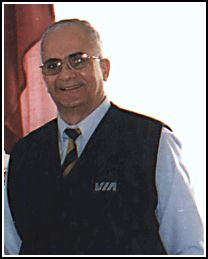 Man standing with tinted-glasses and wearing a blue vest with VIA on the chest.
