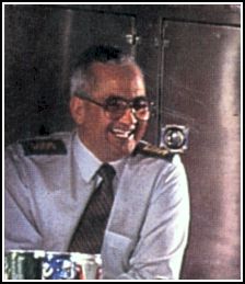 Man laughing, wearing tinted glasses and a white shirt and tie.