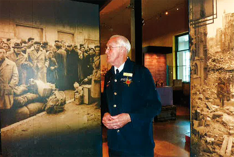 A man in tour guide uniform stands in front of a museum exhibit.