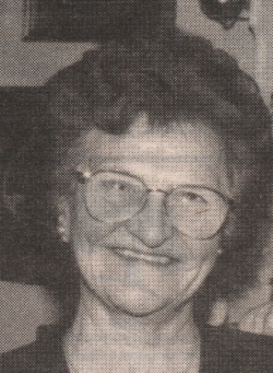 Portrait photograph of an older woman with short brown hair and wearing glasses.