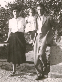 Man and woman standing against stone fence, with little girl on fence between them.