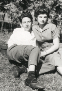 Man and woman laying back on grassy area, with bushes behind.