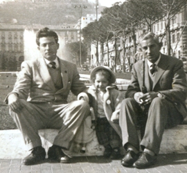 Two men seated on stone blocks in city square with small child between them.