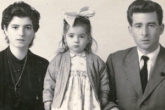 Young girl with big bow on head, mother and father on either side.