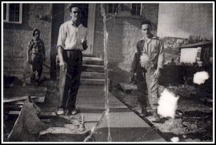 Old, cracked photo showing three men laboring on cement walk outside house.