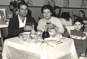 Young man, woman and child sitting at the dinner table loaded with plates and glasses.