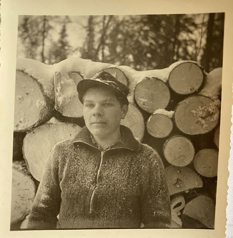 Young man stands in frot of snow-covered logs.