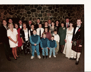 Recent family photograph of several adults and children, taken in front of a stone wall.