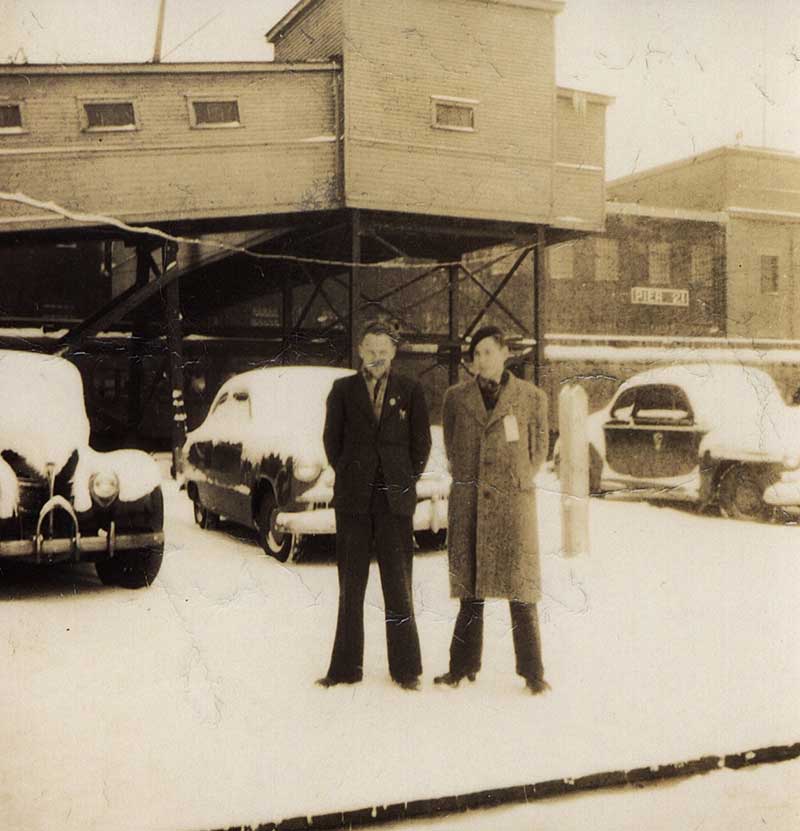 Two young men are standing in snow in front of Pier 21.