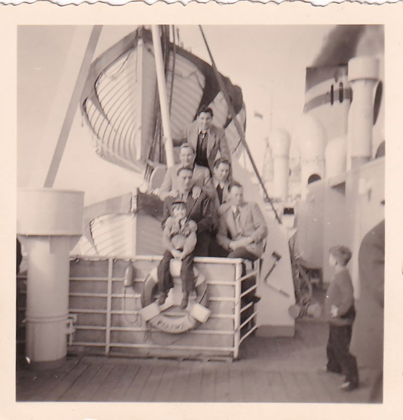 Young men are all seated near a life preserver on the deck of a ship.