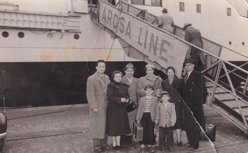 Family stand in front of a ship, next to the gangway.