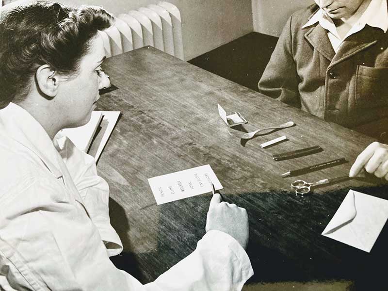 Two young ladies are sitting at a table; there are scissors and paper on the table.