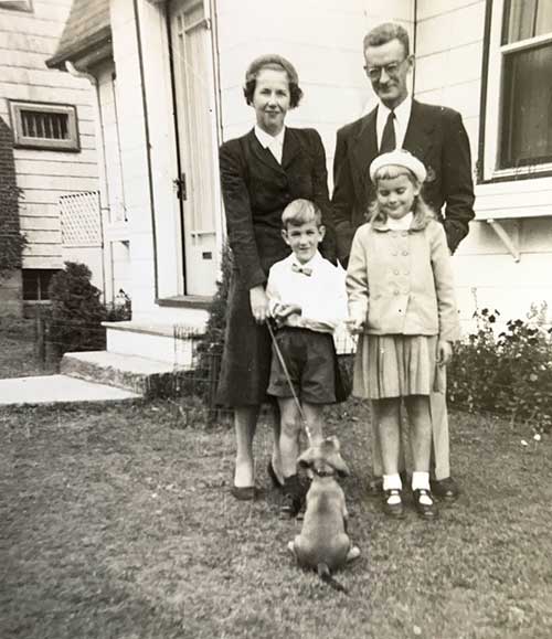 Couple with two children and a dog stand in front of their house for a photo.