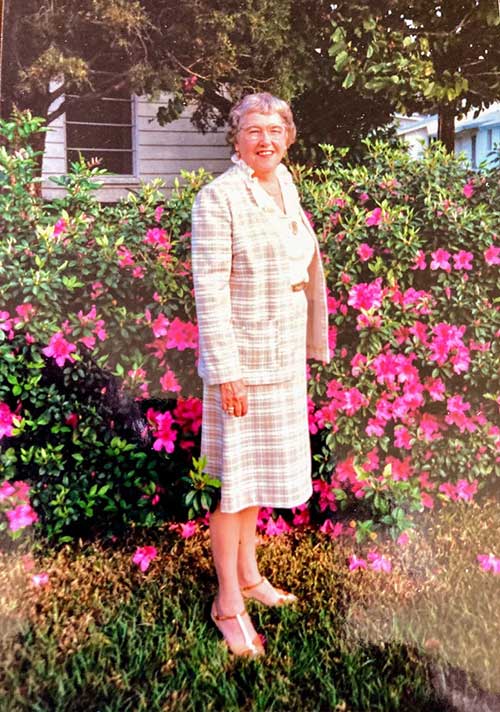 A well-dressed young woman is standing in front of a flowery garden.
