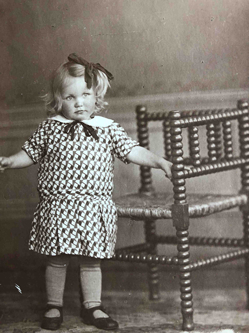 A little blonde girl with a bow in her hair poses for the camera.