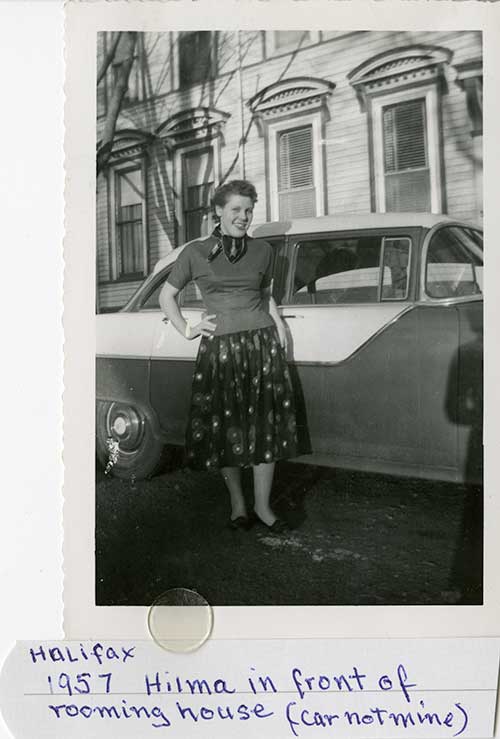 Black and white photo of young woman in standing in front of old car.