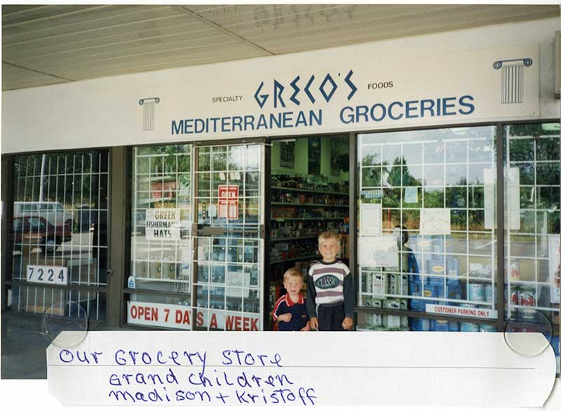 Two young boys standing in entrance way of a Greek grocery store.