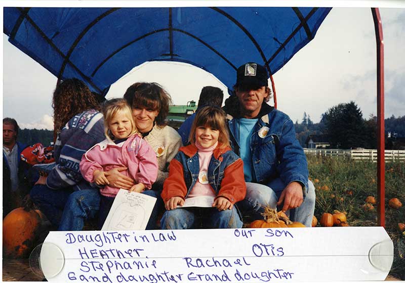 Woman, man and two young girls sitting on a wagon in a pumpkin patch.