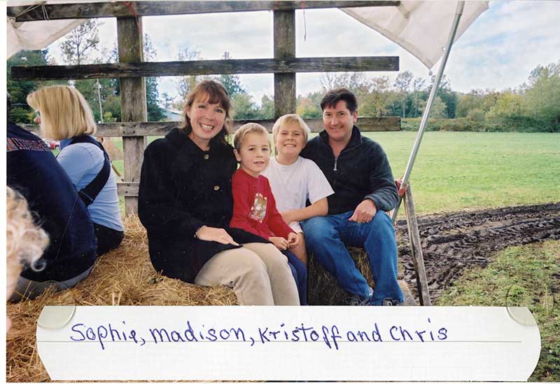 Woman, man and two young boys sitting on a hay wagon in a pumpkin patch.