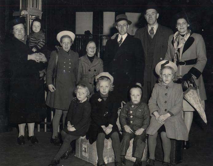 Well-dressed group of people with luggage sitting and standing for photo.