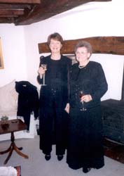 Mother and adult daughter, both wearing black dresses and holding wine glasses.