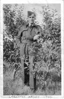 Young man in a sailor uniform, standing in front of small trees.