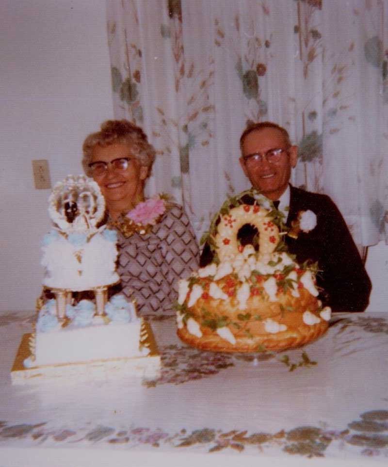 An older couple sit behind two anniversary cakes.